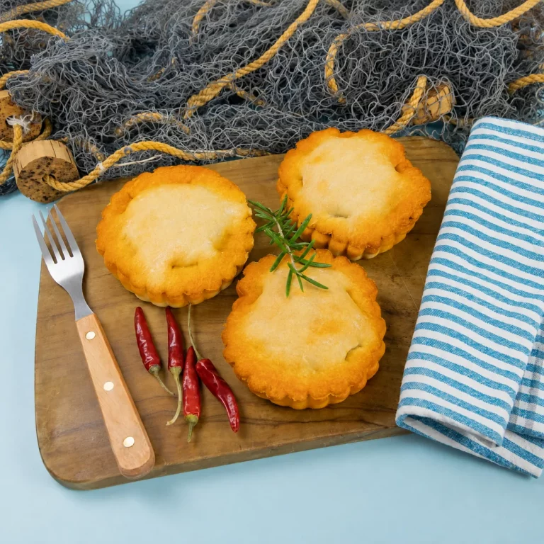 Tielles sétoises présentées sur une planche avec fourchette, piments et décor marin.
