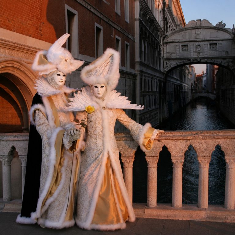 Deux personnages masqués en costumes blancs devant le pont des Soupirs à Venise