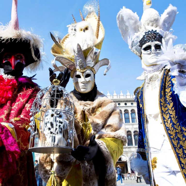 Trois personnages masqués en costumes colorés sur la place Saint-Marc à Venise
