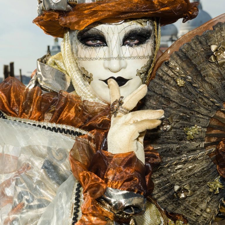 Gros plan sur un masque vénitien accompagné d’un éventail noir et doré