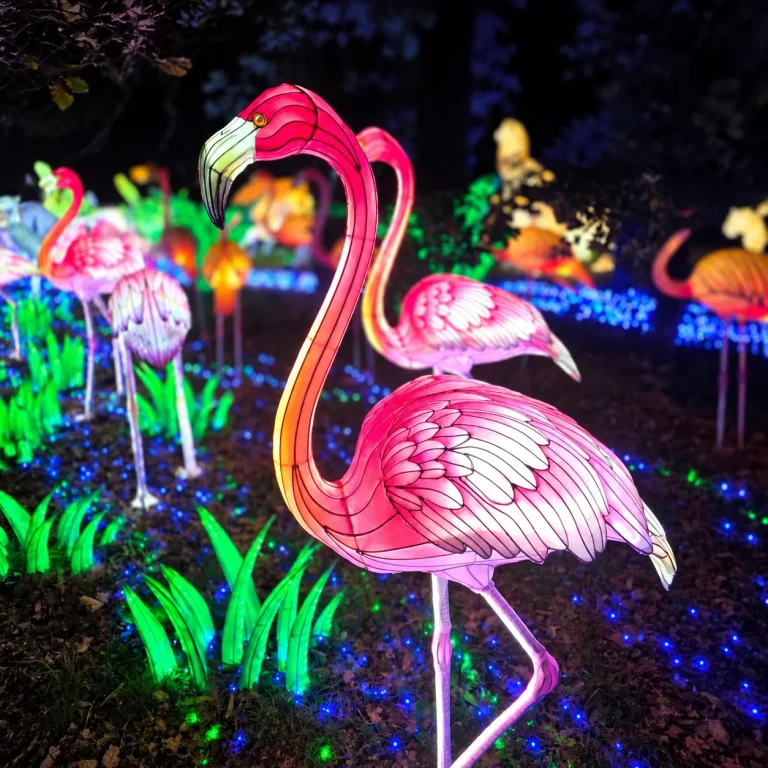Lanternes en forme de flamants roses entourées de végétation lumineuse et de lumières bleues dans la nuit.